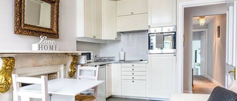 A compact kitchen with white cabinets, a white dining table, and a sofa.