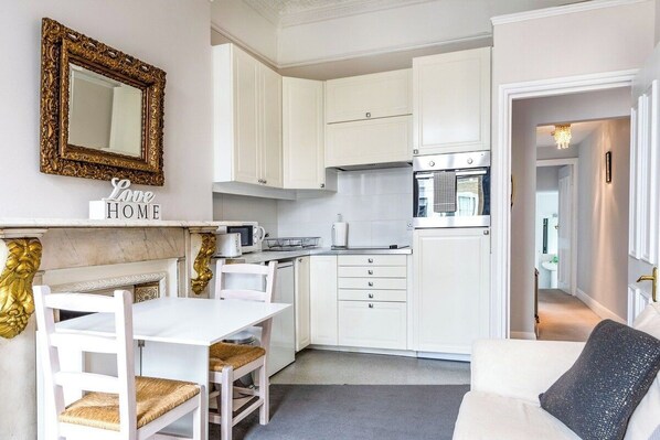 A compact kitchen with white cabinets, a white dining table, and a sofa.