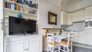 Een moderne keuken met witte kasten, een eettafel met stoelen en een flatscreen televisie boven de aanrechten.