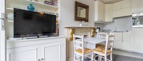 A modern kitchen with white cabinetry, a dining table with chairs, and a flat-screen TV mounted above the counter.