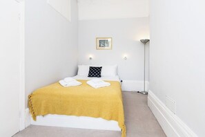 A hotel room with a bed, a bedside lamp, a picture on the wall, and a yellow throw blanket.