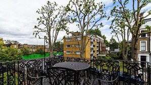 Een balkon met een ronde tafel en stoelen, omgeven door een smeedijzeren hekwerk.