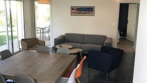 Una sala moderna con una mesa de comedor de madera, un sofá gris y un sillón azul. Hay un cuadro en la pared y una lámpara colgante.