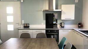 Cocina moderna con una mesa de comedor de madera y sillas grises, horno empotrado y campana extractora de acero inoxidable.
