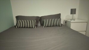 Ein Bett mit einer grauen Bettdecke und zwei schwarz-weißen Kissen.
