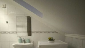 Ein kleines, kompaktes Badezimmer mit einem Waschbecken auf Säule, einer weißen Waschmaschine, einem Spiegel und einer kleinen Pflanze.