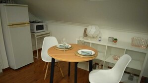 Ein kleiner Essbereich mit einem Holztisch, zwei weißen Stühlen, einem weißen Kühlschrank, einer Mikrowelle und einem weißen Regal mit Dekoration.