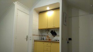 Eine kompakte Küche mit gelben Schränken, einem kleinen Mülleimer und einer Steckdose an der Wand.
