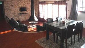 A dining area with a stone wall, a fireplace, a TV mounted on the wall, and a window with curtains. - Louro's Villa in Vila Nova (Coimbra)