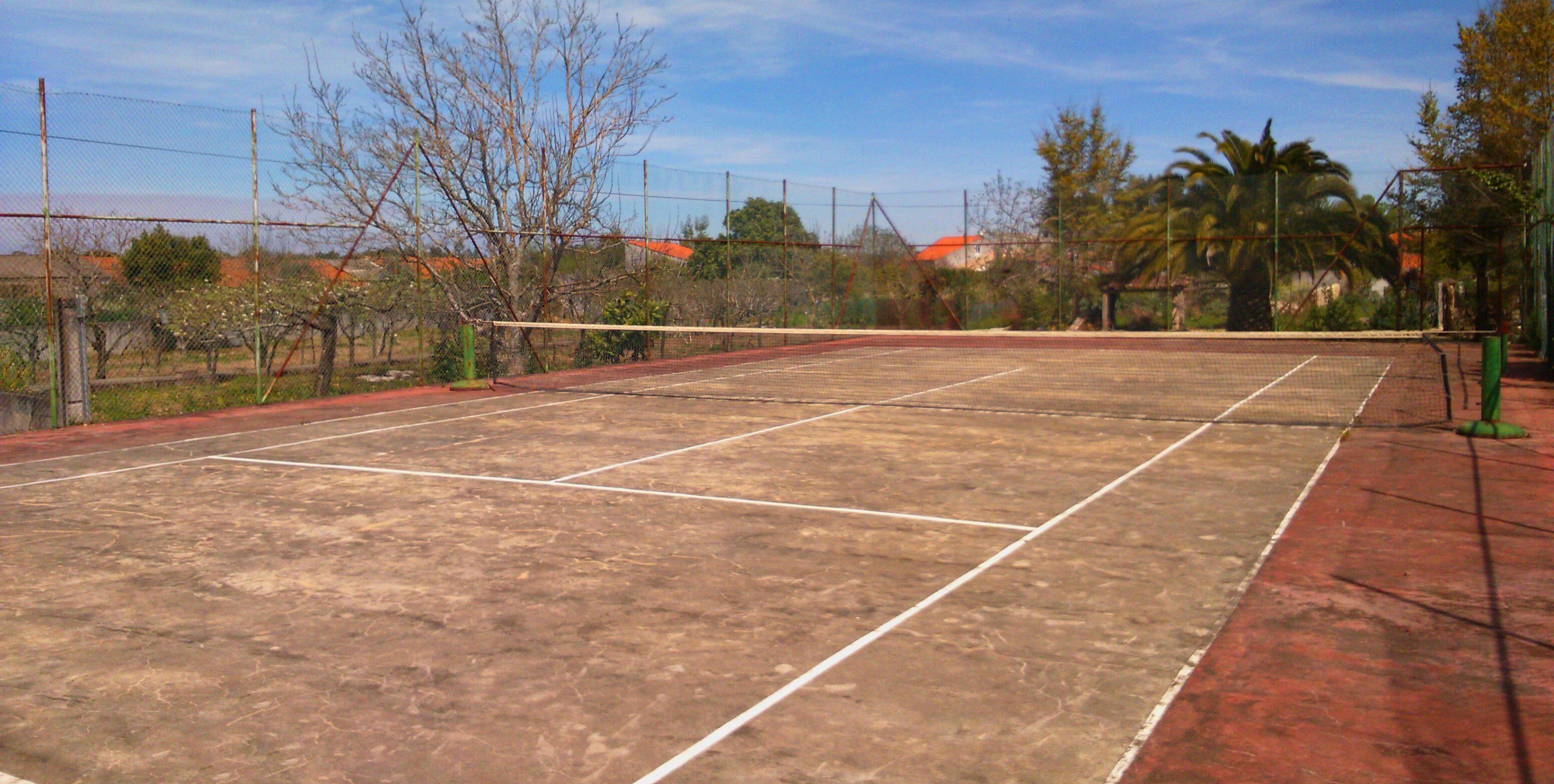Un court de tennis en plein air, doté d’un filet, entouré d’une clôture et d’arbres.