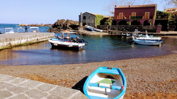 A coastal harbor with boats docked, a stone building, and a paved walkway.