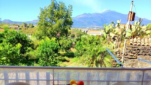 A balcony with two white plastic chairs and a table covered with a colorful tablecloth. A fruit basket with oranges and lemons is on the table.