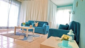 A living room with a blue sofa, a white coffee table, and a small table with a vase of flowers.
