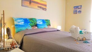 A bedroom with a bed, pillows, a nightstand, a lamp, and a wall with a painting.