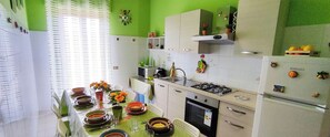 A kitchen with a dining table set for four, a microwave, stove, and refrigerator. - House with a panoramic view of Mount Etna near the sea (Acireale)