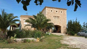 A stone building with a central courtyard, palm trees, and a statue. - Villa 18 pax with large pool close to Es Trenc (Campos - Sa Rapita)