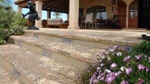 A stone building with a covered patio, steps leading to a seating area, and a statue. - Villa 18 pax with large pool close to Es Trenc (Campos - Sa Rapita)