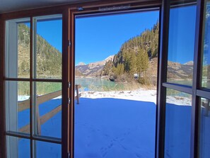 Una habitación con un amplio ventanal que ofrece vistas a un paisaje nevado, una terraza de madera y montañas al fondo.