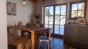 A dining area with a wooden table, chairs, and a bench. There is a window with a view of mountains and a lake.