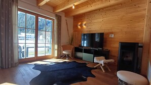 A spacious living room with a large wooden ceiling, a black leather rug, a television, and a fireplace.