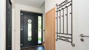 A hallway with a dark wooden door, a light-colored wall with a metal rack, and a wooden door frame. - Frida - Family vacation home, WLAN free, sauna, fireplace, 8 persons (Fehmarn)