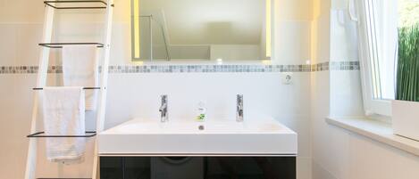 A bathroom with a white sink, two faucets, a mirror, and a towel rack.