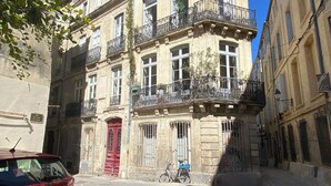 Un edifici de diverses plantes amb balcons, un cotxe vermell a la façana i una bicicleta.