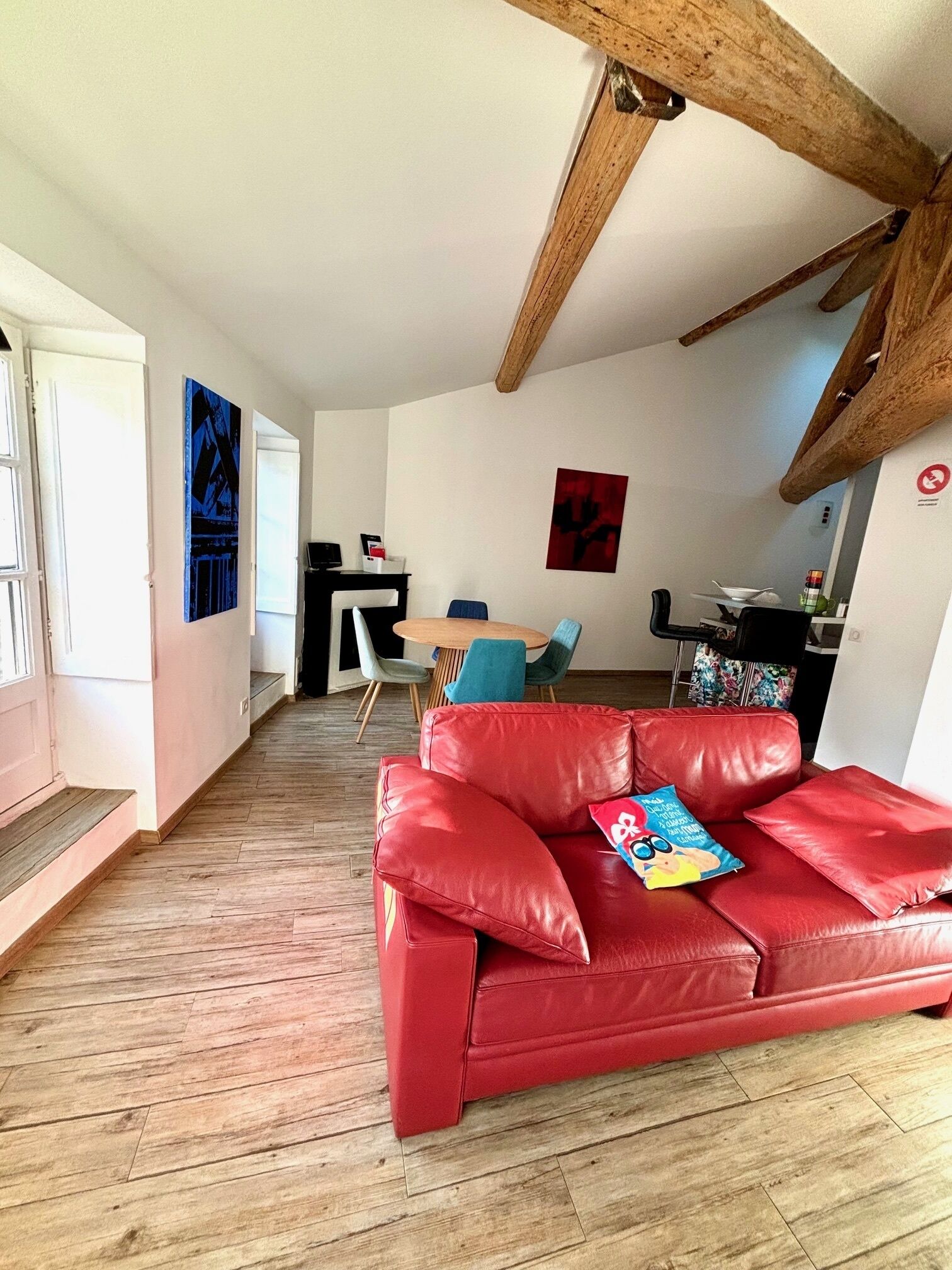 A spacious living area with a red leather sofa, wooden flooring, and a dining area with blue chairs.