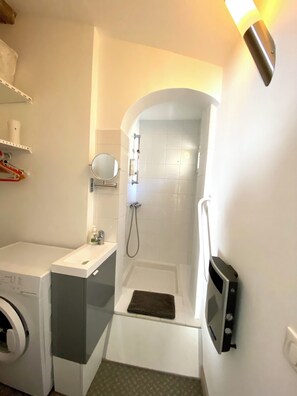 A compact bathroom with a washing machine, a small sink, a shower area, and a microwave. - Calm, central and sunny, with unobstructed view (Montpellier)