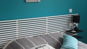 A bedroom with a teal wall, a bed with striped bedding, and two pillows. There are two wall-mounted artworks depicting landscapes. - Little parenthesis in Trinité-Sur-Mer (La Trinité-sur-Mer)