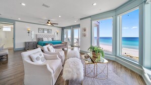 Un salon spacieux doté d’une grande fenêtre donnant sur une plage, d’un ventilateur de plafond et d’un coin salon confortable.