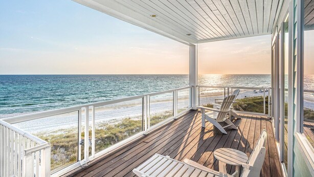 Une terrasse en bois avec une balustrade donnant sur une plage et l’océan.