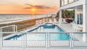 Une piscine offrant une vue sur l’océan et la plage au coucher du soleil.