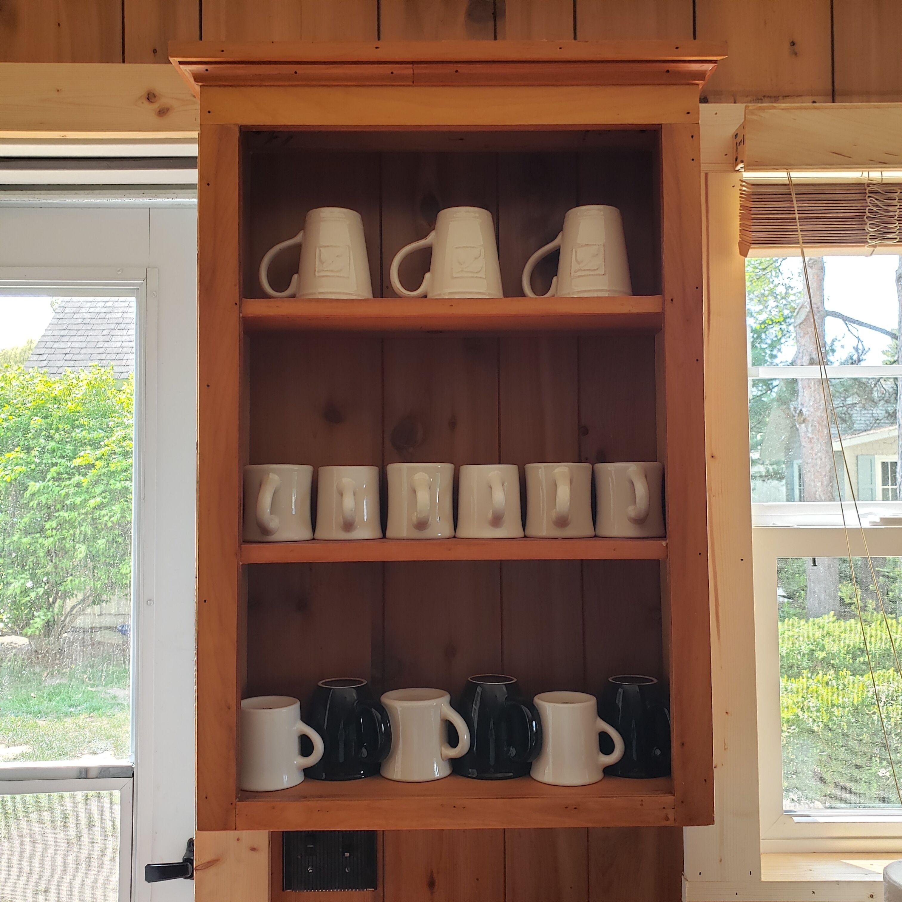 A wooden cabinet with shelves holding white and black mugs.