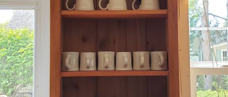 A wooden cabinet with shelves holding white and black mugs.