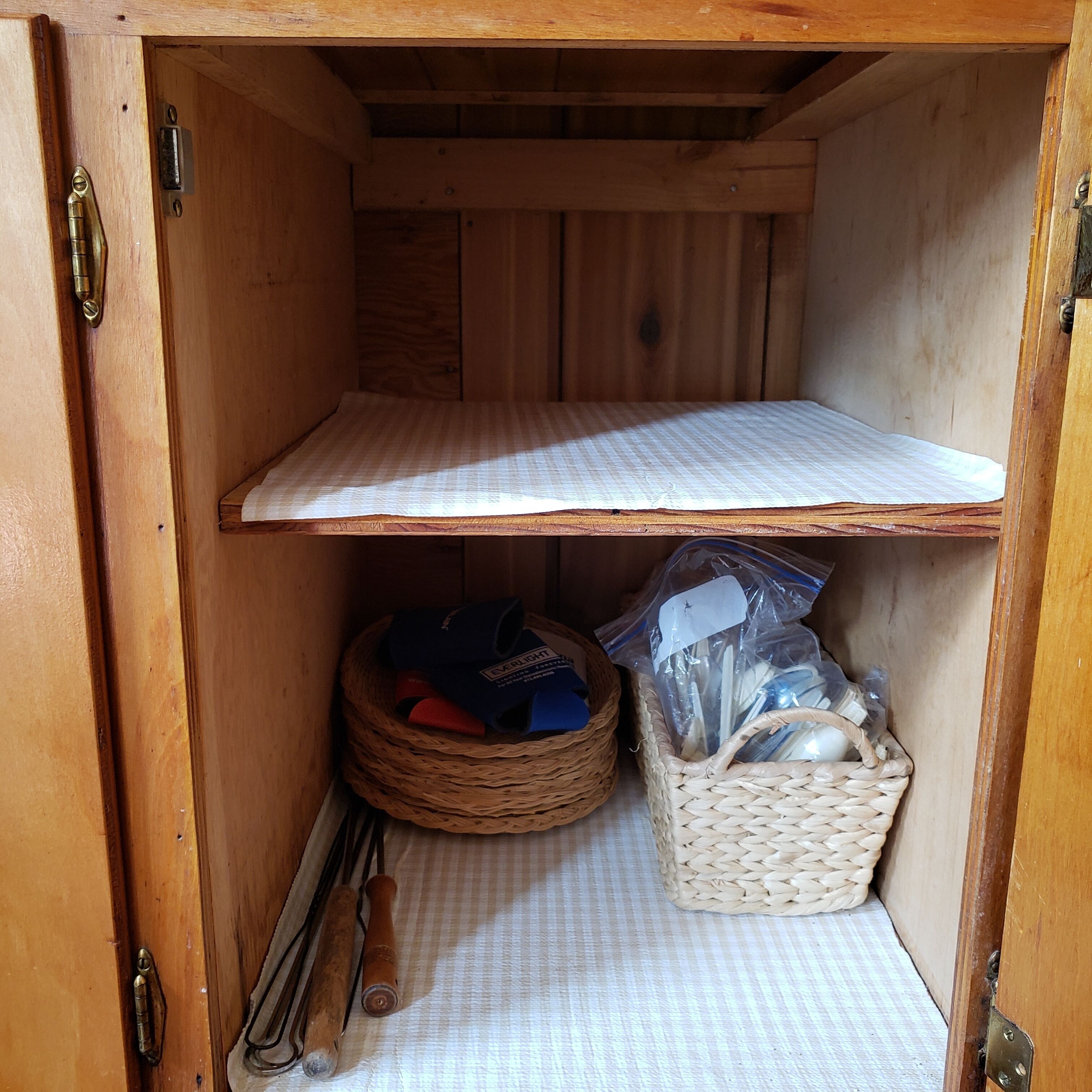 A wooden cabinet with a checkered mat on the floor, a woven basket, and a metal shelf.