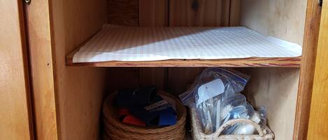 A wooden cabinet with a checkered mat on the floor, a woven basket, and a metal shelf.
