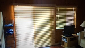 A room with wooden walls, a sliding glass door with blinds, a television on a wooden stand, a sofa, and a small table. - Home on the lake. Walk out your door for Swimming, boating or morning coffee. (Mears)