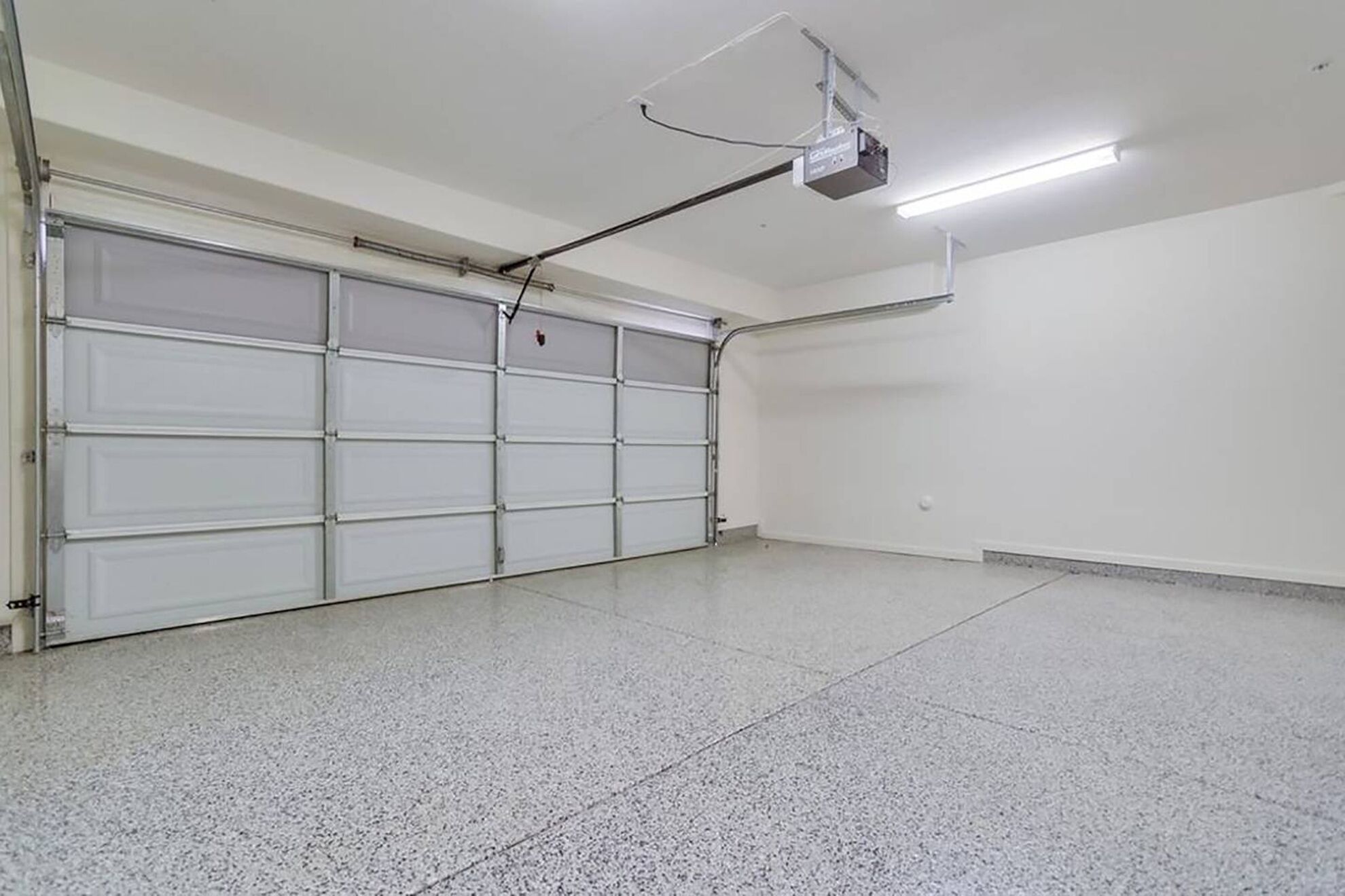A clean, empty garage with a white garage door and a ceiling-mounted projector.