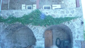 Ein Steinhaus mit zwei Rundbögen, einer Holztür und einem Metallgitter.