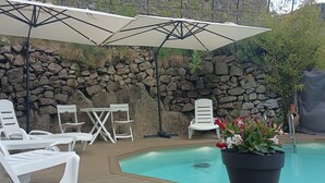 Ein Poolbereich mit weißen Liegestühlen, einem Tisch und Sonnenschirmen.