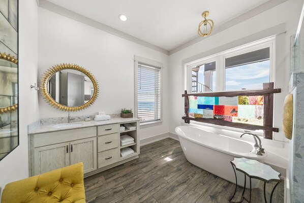 A modern bathroom with a freestanding bathtub, a vanity with a marble countertop, and a large mirror with a gold frame.