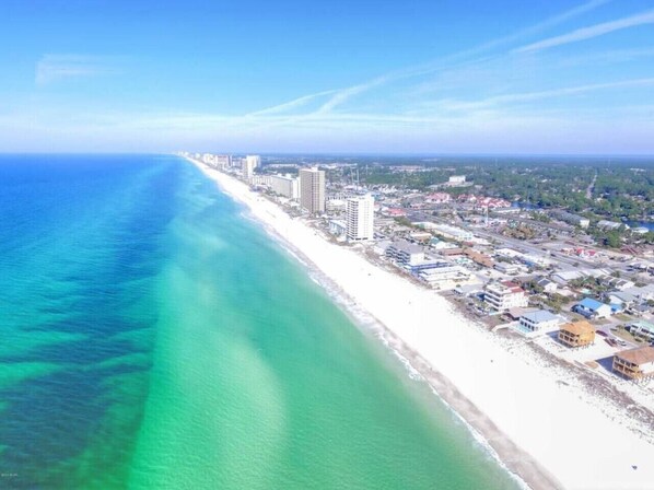 An aerial view of a coastal city with a long beach, high-rise buildings, and a clear blue sky.