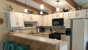 A kitchen with white cabinets, a black stove, a microwave, and a refrigerator. There are three green stools and a sink with a faucet. - On Golf Course, 4 Bedrooms, 3 bathrooms, Sleeps 10 (Angel Fire)