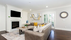 A living room with a fireplace, a sofa, a coffee table, and a TV mounted on the wall. - Stunning Home near Piedmont Park & Ansley Park - Convenience & Luxury! (Atlanta)