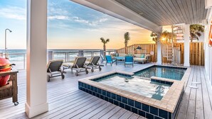 A poolside area with a view of the ocean, lounge chairs, and a hot tub.