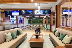 En bowlinghal med siddepladser, flere skærme der viser sport, og et træloft.