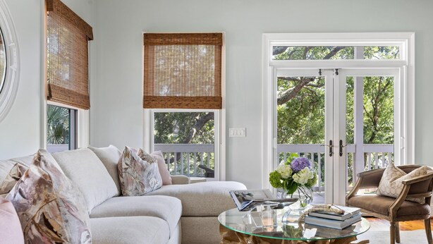 A modern living room with a sectional sofa, a glass coffee table, and a view through large glass doors to the outdoors. - Private heated pool + 1 block from beach + Pet Friendly (Folly Beach)