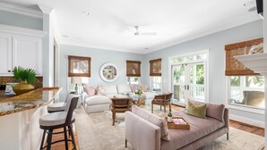 A spacious living room with a large window, a sofa, a coffee table, and a bar area with stools. - Private heated pool + 1 block from beach + Pet Friendly (Folly Beach)