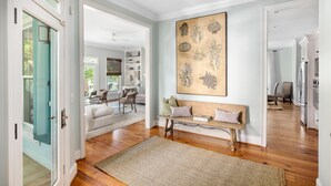 A spacious living room with a wooden bench, a large abstract painting, and a view into the adjacent dining area. - Private heated pool + 1 block from beach + Pet Friendly (Folly Beach)
